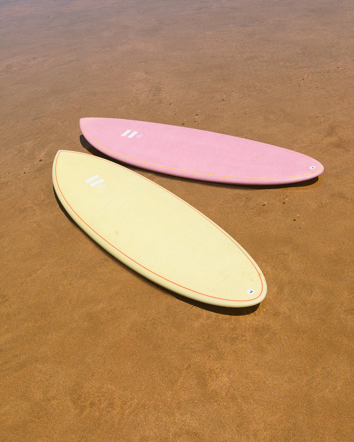 Indio Racer sand and pink surfboards showing its shapes in shallow water